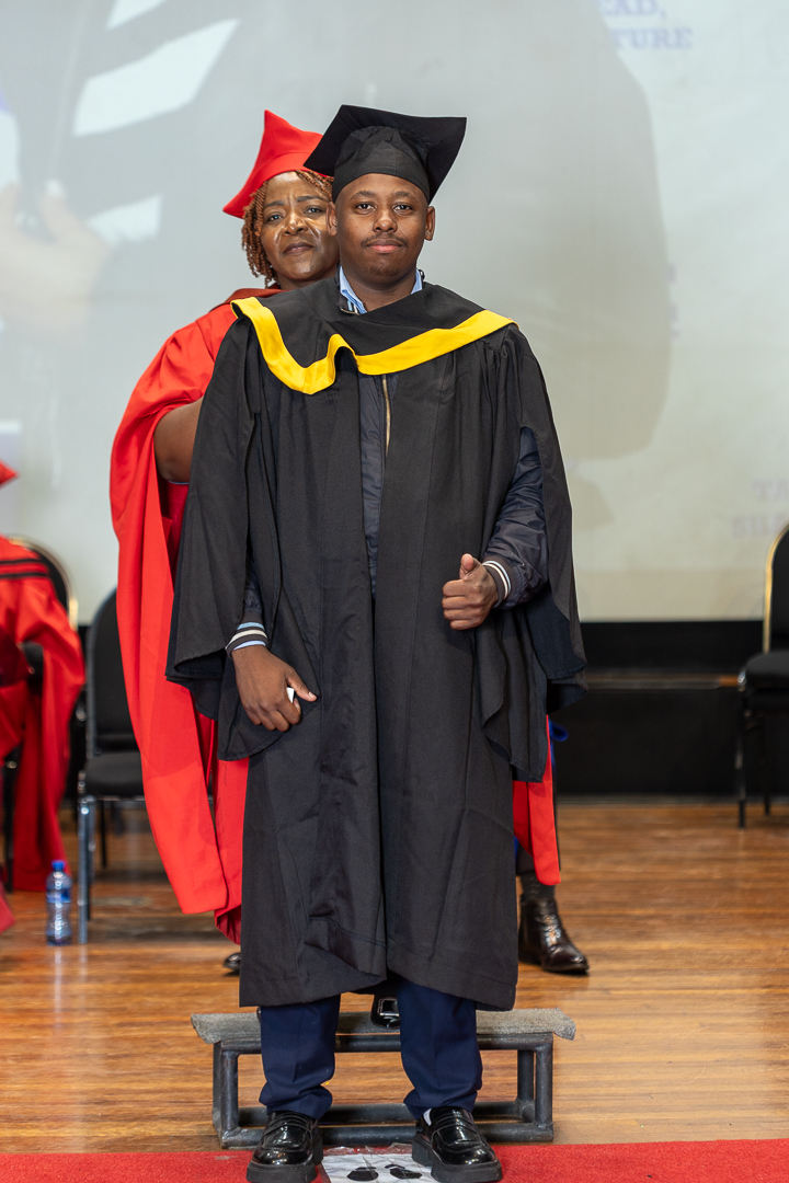 Graduate receives a certificate on stage during the graduation ceremony as faculty members look on.